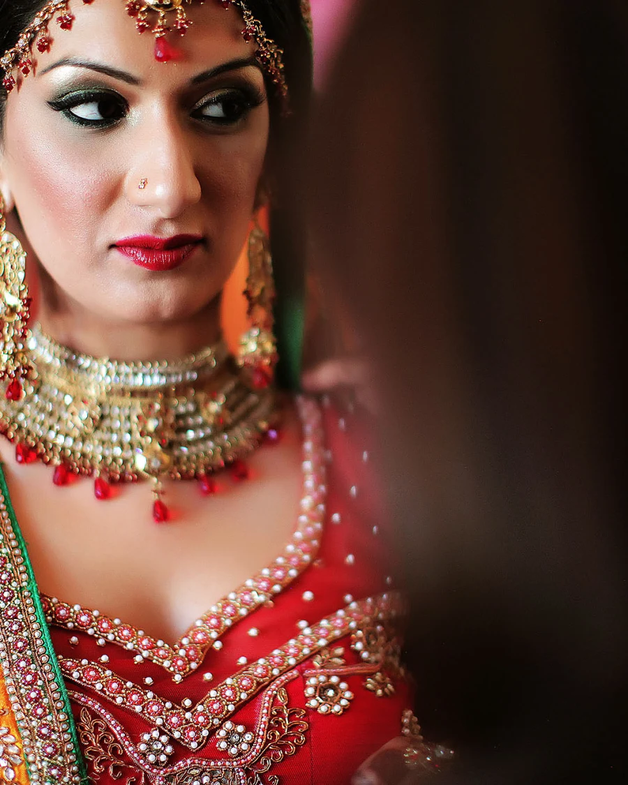 A bride in a red and gold lehenga with a heavy necklace and maang tikka