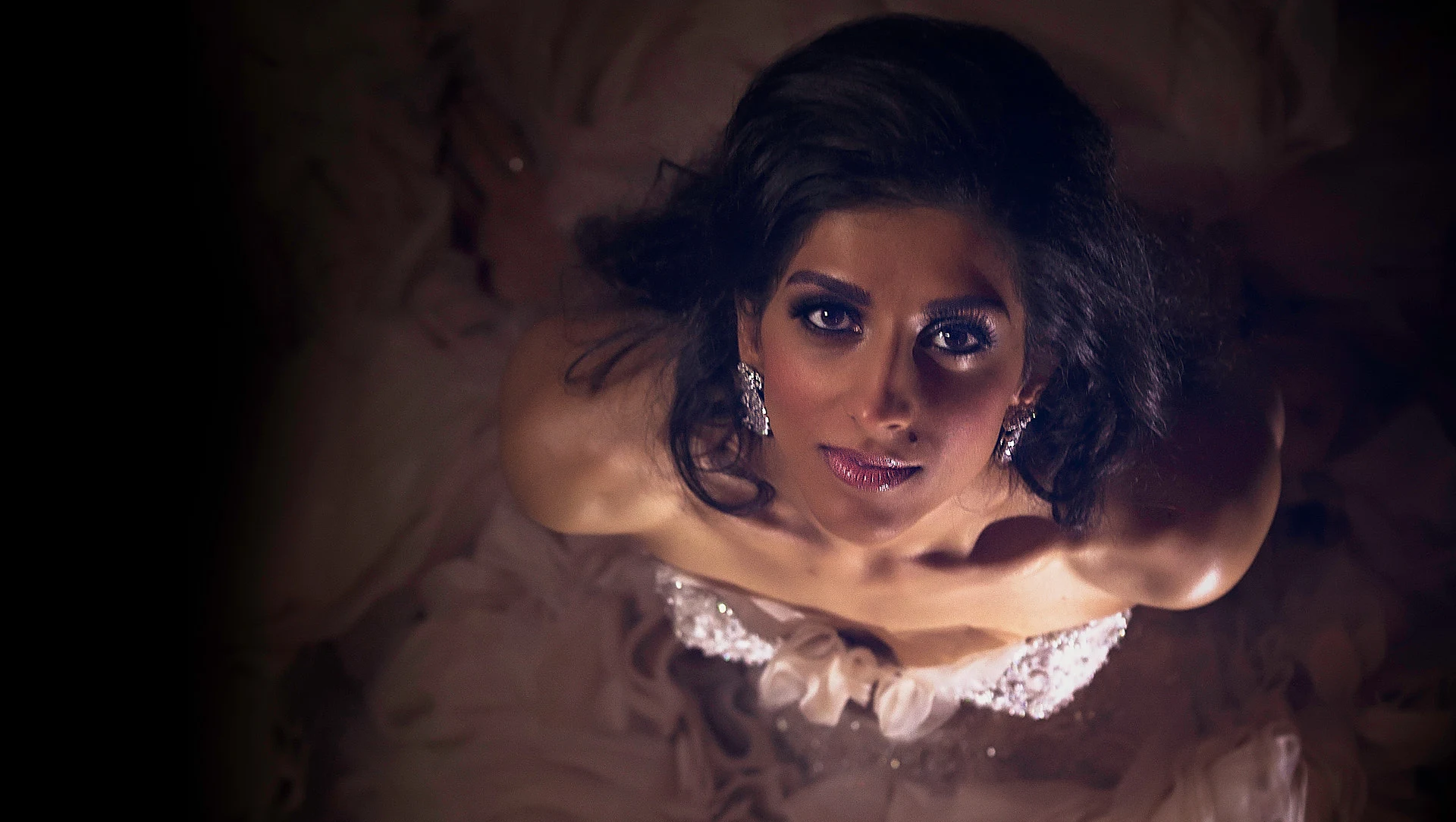 Looking down on a bride gazing up from a cloud of ruffled fabric in warm low light.