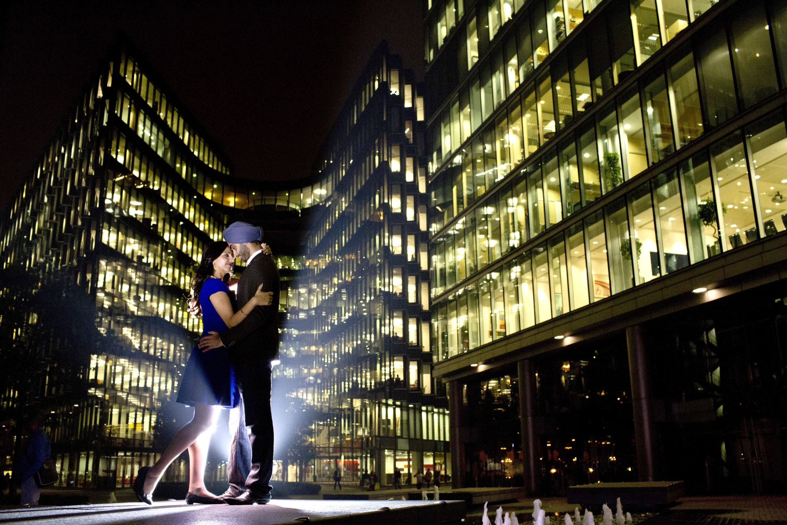 Bride and groom at night beside a lit glass office tower in the city