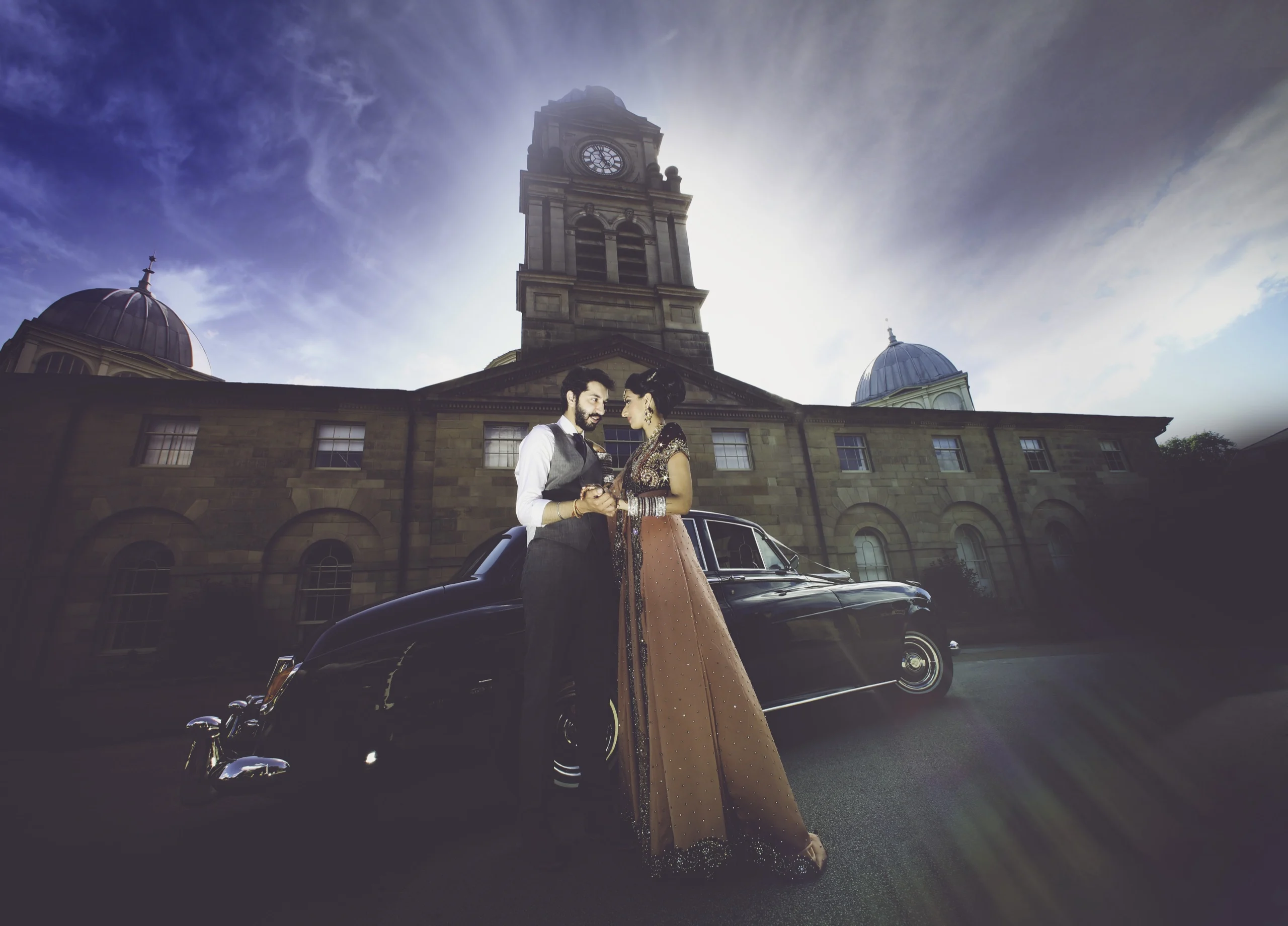 Bride and groom with a vintage car outside a historic city building