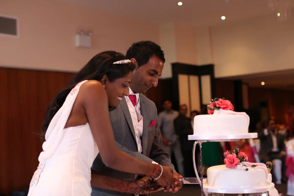 A bride and groom laugh as they cut their wedding cake