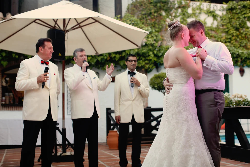 A bride and groom dance on a terrace as three singers perform beside them