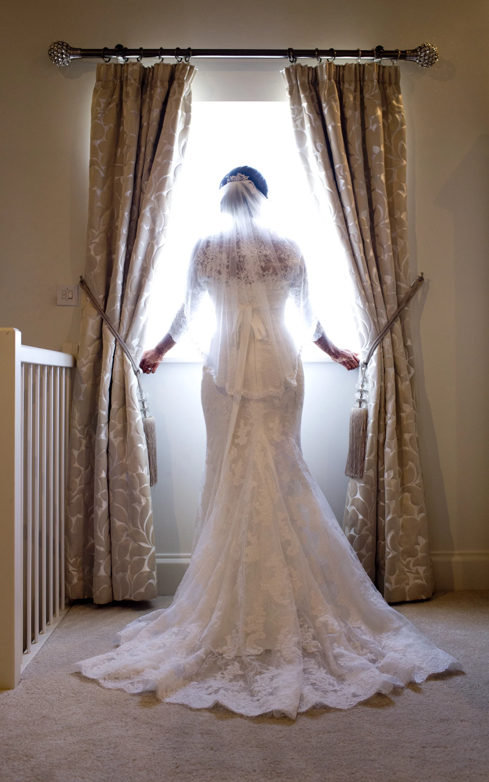 Bride silhouetted at a tall window in her wedding dress