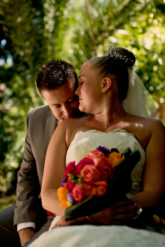 A groom embraces his bride in a sunlit tropical garden
